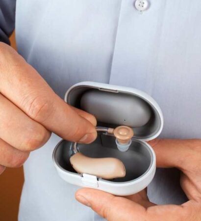 Person holding a hearing aid and charging case.