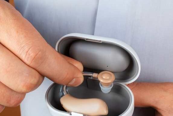 Person holding a hearing aid and charging case.