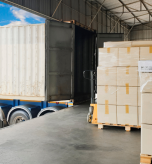 Pallets of packaged goods beside an open freight container at a warehouse