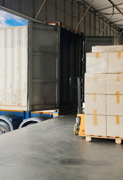 Pallets of packaged goods beside an open freight container at a warehouse