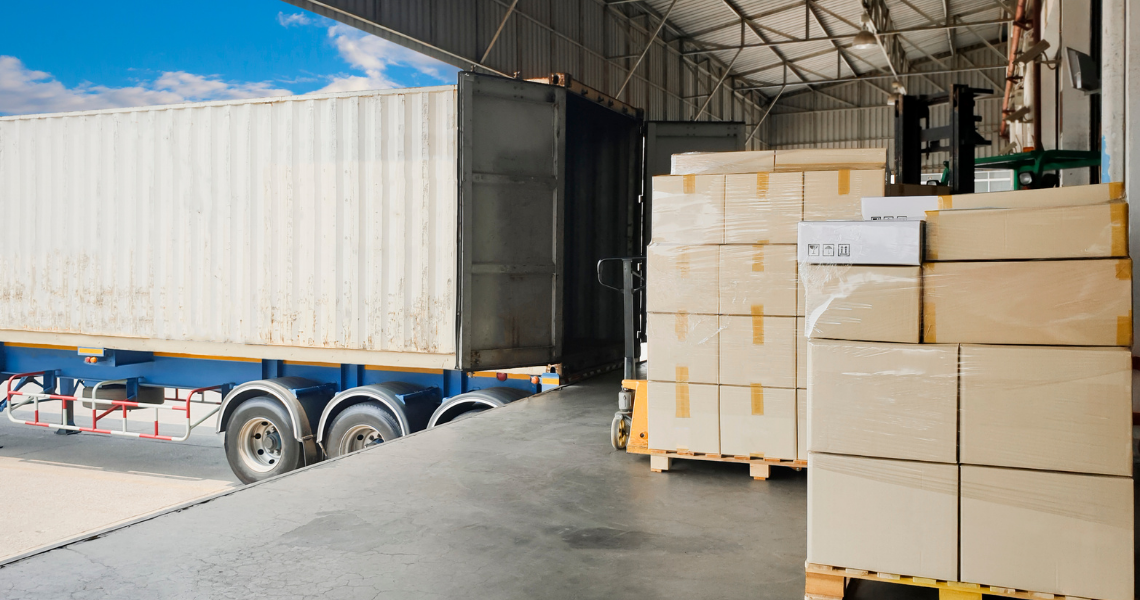 Pallets of packaged goods beside an open freight container at a warehouse